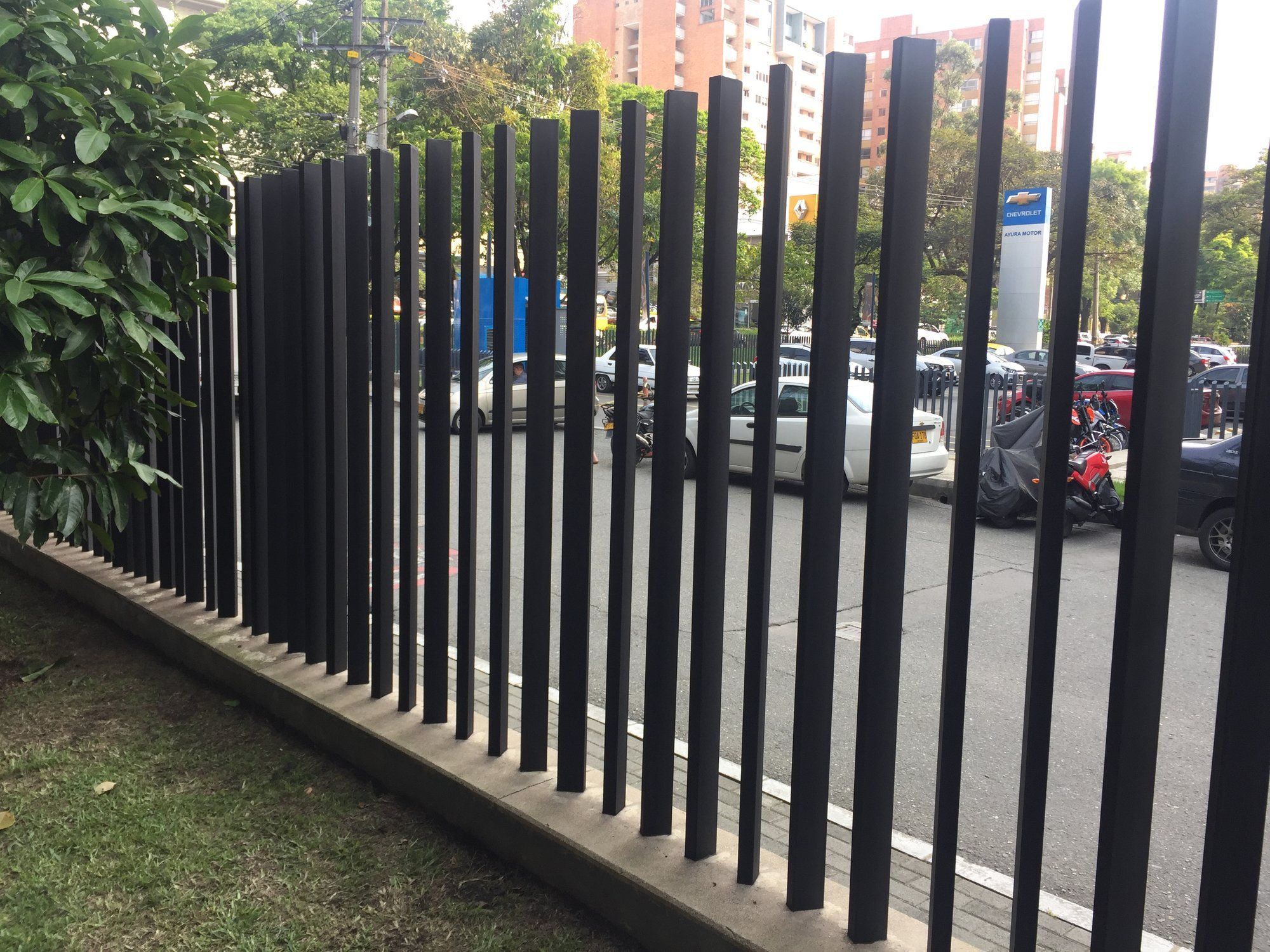 Cerramiento en platinas verticales grafito junto a una vía con edificios