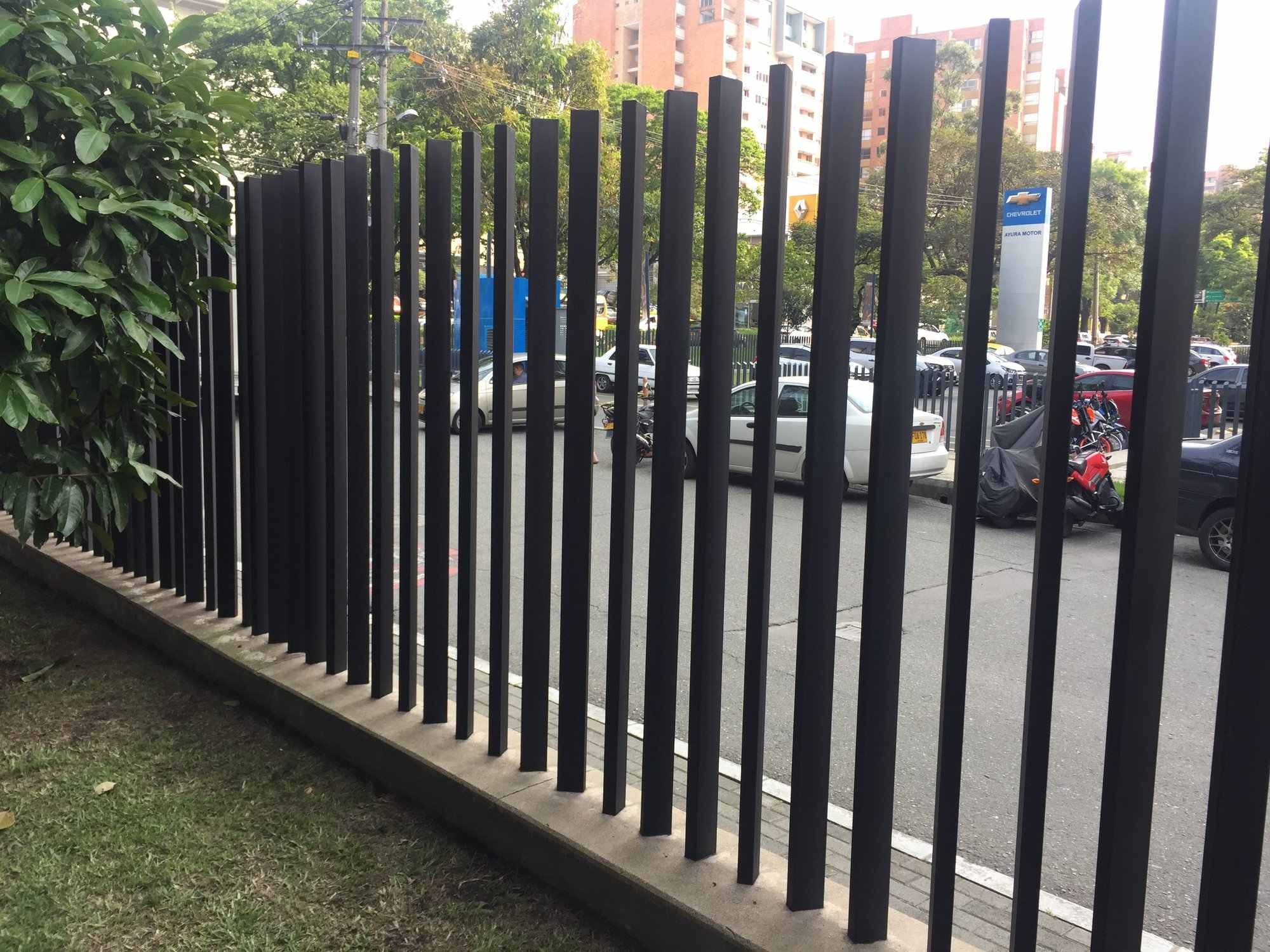 Cerramiento en platinas verticales grafito junto a una vía con edificios