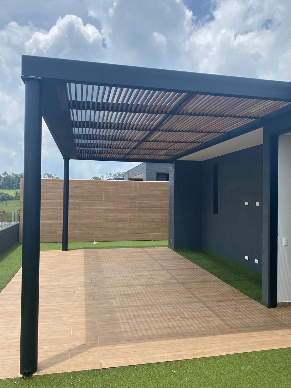 Pérgola en acero negro con listones de madera sobre una terraza con piso de madera