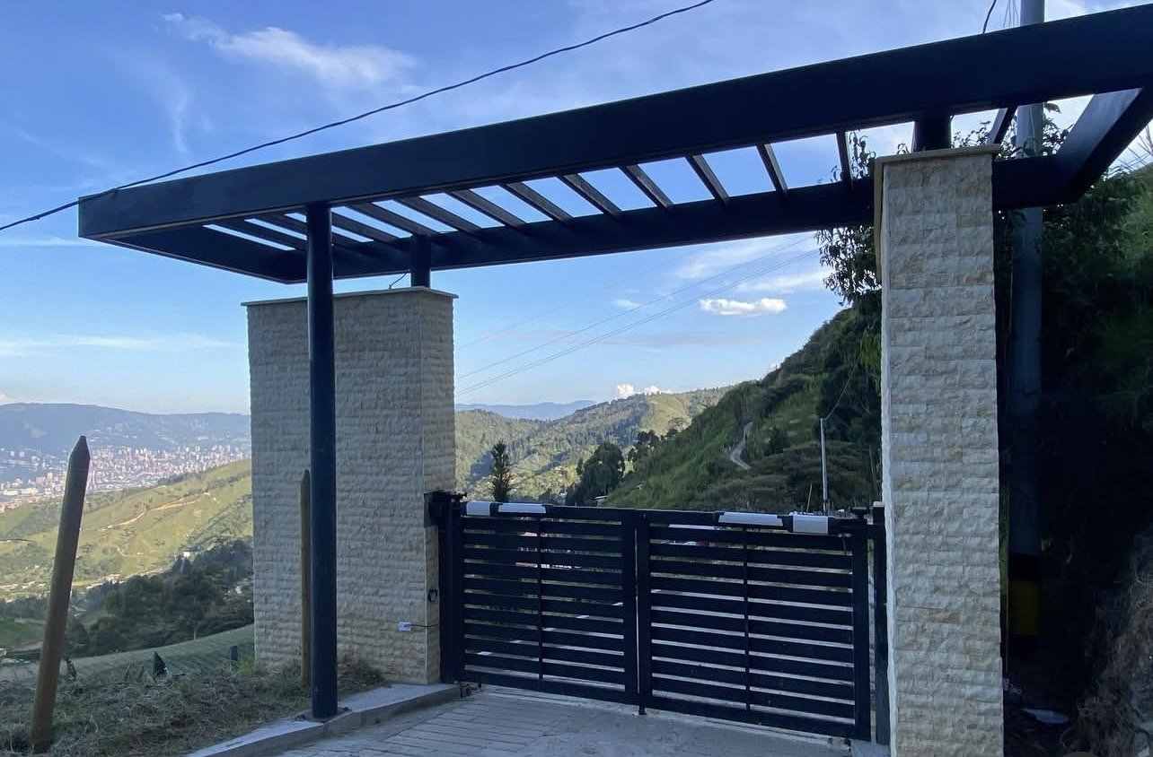 Pórtico en acero con pérgola y portón automático de dos hojas, con la ciudad al fondo